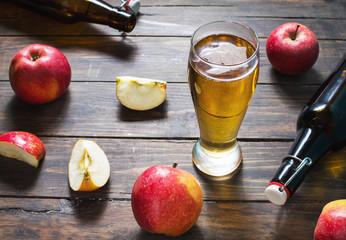 Glass of cider with apples and bottle on rustic wooden background
