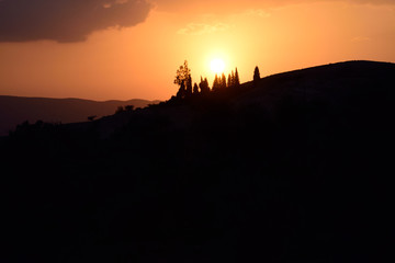 Sonnenuntergang in rotem Feuer über Berghang mit kleiner Baumgruppe