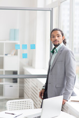 Serious businessman in elegant suit looking at camera while standing by window in office