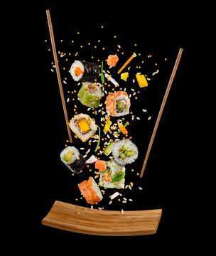 Flying pieces of sushi with wooden chopsticks and plate, isolated on black background.