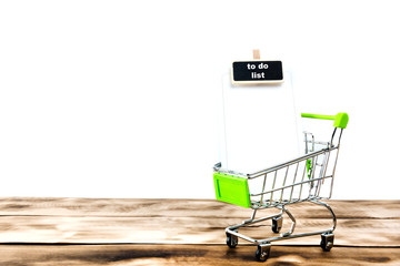 Shopping list in metal shopping cart on wooden background.