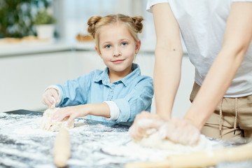 Obraz na płótnie Canvas Adorable little girl helping her mother to make and knead self-made dough for homemade buns