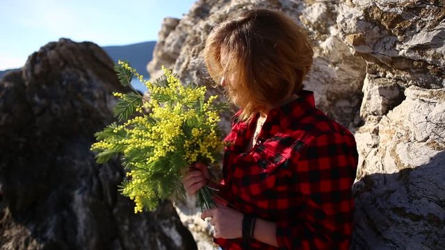 A woman with a bouquet of mimosa near a stone on the seashore