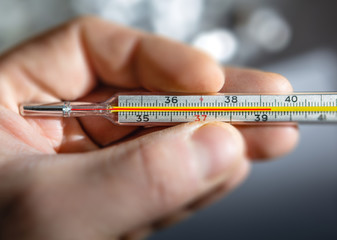 Traditional medical thermometer for measuring body temperature in hand.