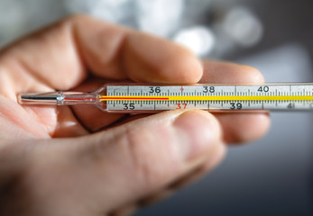 Traditional medical thermometer for measuring body temperature in hand.