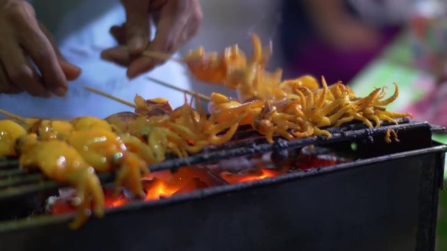 Traditional street food of Thailand. Cooking small squids on the grill at night streetfood fair