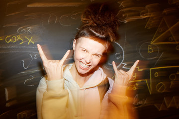 Pretty girl with rock gesture standing by school blackboard with chalk notes