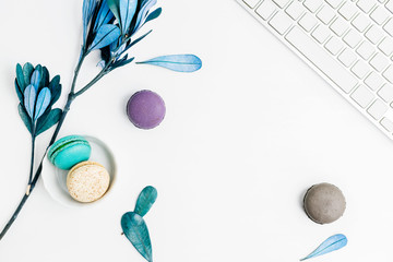 Top view flat lay colorful macarons with keyboard and blue leaves. Creative dessert concept