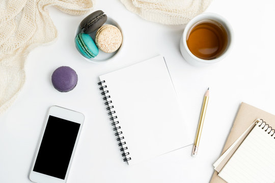 Top view flat lay Blank notebook and cell phone mockup with macarons and tea cup. Art, writing concept. Text space