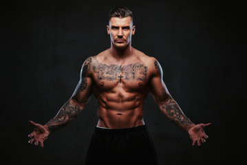 A muscular tattooed man on a dark background.