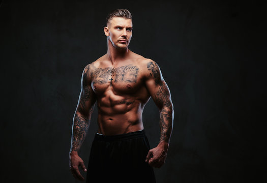 A muscular tattooed man on a dark background.