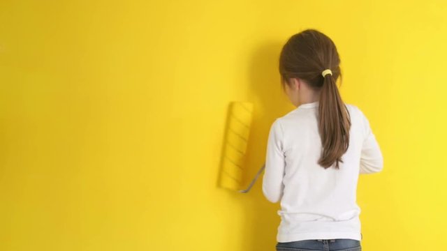funny little girl gingerly paints the walls with a roller in the room