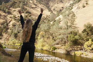 teen girl standing with raised hands near merced river on warm autumn day