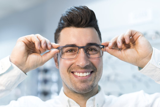 Man trying on glasses in optical store while smiling happy