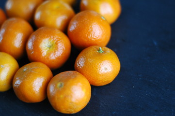 Unpeeled mandarins on a dark background with hard light.