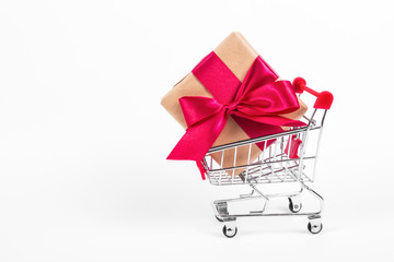 Gift box with  bow in shopping trolley. Shopping cart with large gift box on white background