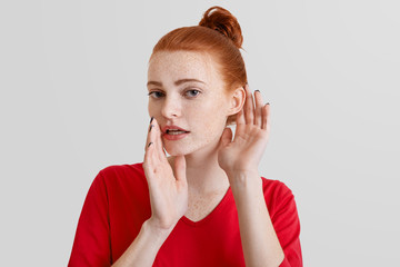 Beautiful foxy woman tries to overhear or eavesdrop someonen`s gossiping, keeps hand near ear,...