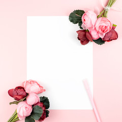 Blank paper card with pen, red and pink flowers frame on pastel background, copy space.