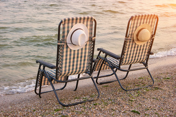 Two checkered beach chairs. Sun hats attached with string to the backrest.