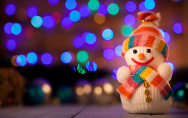 Snowman in a hat and scarf on a table in the background of a bokeh
