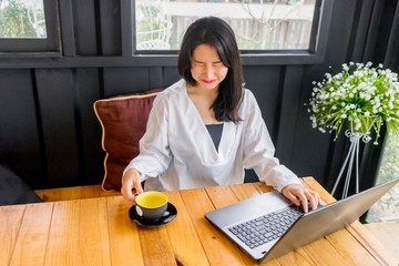 An Asian girl in white shirt plays notebook on wooden table in black room.