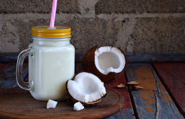 Coconut milk in bottle with broken coco on wooden background. Delicious milk cocktail. Copy space