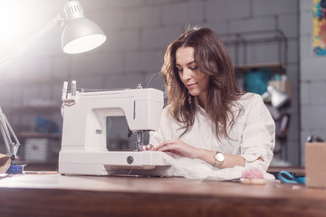 Attractive Caucasian seamstress working stitching with sewing machine at her workplace in studio...