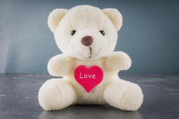 White toy teddy bear with heart on a gray background. The symbol of the day of lovers. Valentine's Day. Concept February 14.