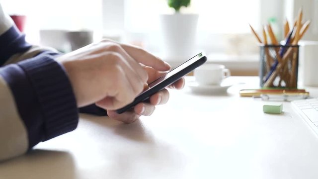 Businessman uses a smartphone and laptop in the office at the workplace. Very smooth dolly shot. 4K video with shallow depth of field focus on hands with phone.
