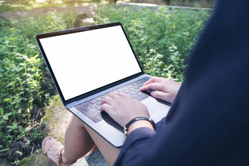 Mockup image of business woman using and typing on laptop with blank white desktop screen , sitting at outdoor with nature background