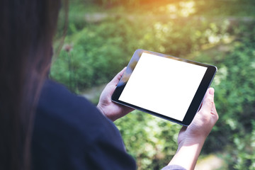 Mockup image of woman's hands holding black tablet pc with blank white desktop screen and green nature background