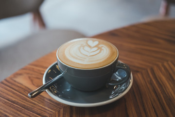 Closeup image of a blue cup of hot latte coffee with latte art on vintage wooden table in cafe