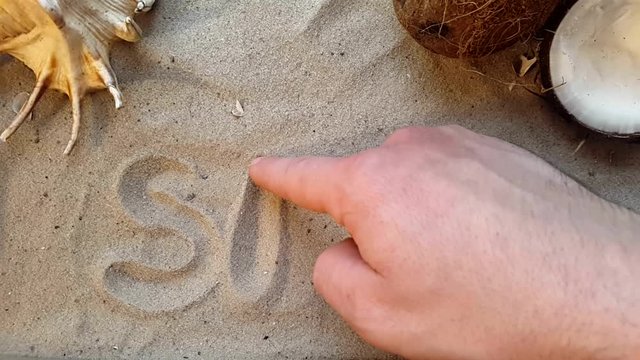 writes the word Spa, on the sand of the beach with a seashell and a coconut