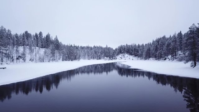 Aerial footage of a drone slowly flying low over snowy white landscape and icy river in Finnish Lapland on a winter day. Oulanka National Park, Ruka, Finland.