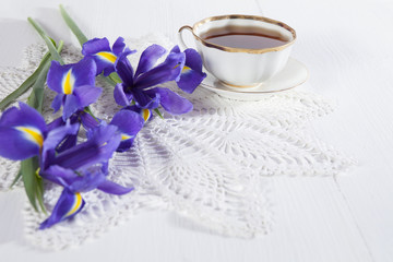 Violet Irises xiphium (Bulbous iris, sibirica) with cup of tea on white background with space for text. Top view, flat . Holiday greeting card for Valentine's Day, Woman's Day, Mother's Day, Easter!