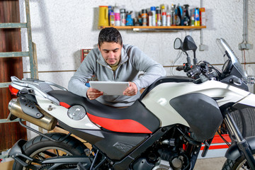 Fototapeta na wymiar young man using a tablet next to motorcycle