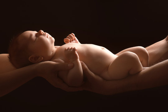 Hands Of Parents Holding Cute Little Baby On Dark Background