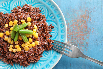 Plate with delicious red rice and vegetables on table