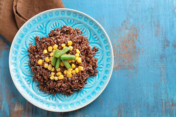 Plate with delicious red rice and vegetables on table