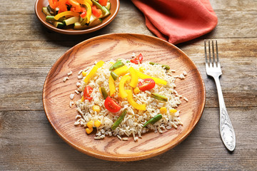 Plate with tasty brown rice and vegetables on table
