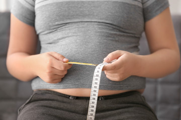Overweight boy measuring his waist at home, closeup