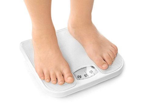 Legs of overweight boy using scales on white background