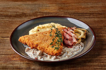 Chicken schnitzel with herb, mashed potatoes and mushrooms sauce on plate on wooden table...