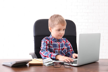 Cute little boy with laptop and money at table indoors