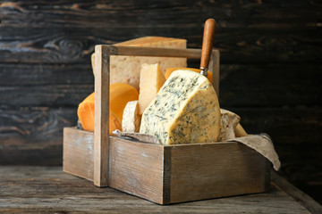 Wooden basket with different kinds of delicious cheese on table