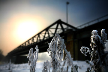 Winter landscape with snow, sun and river bridge in background