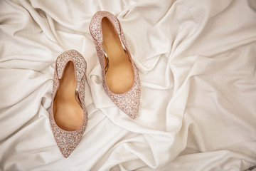 Pair of sparkly female shoes on white fabric, top view