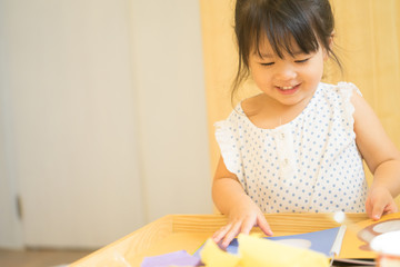 Naklejka premium Cute little girl cutting shapes out of colored paper. Children being creative, developing imagination, creativity, do it yourself concept