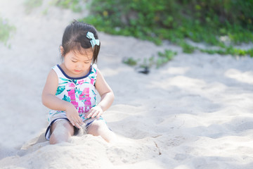 Little asian girl playing white sand on the beach.