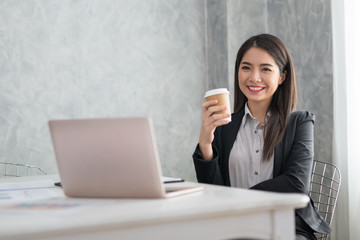 Asian business girl in her workstation at holding coffee cup and smile